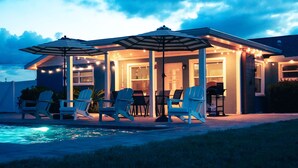 Un espace extérieur aménagé avec des sièges, des chaises et des parasols, une piscine et des guirlandes lumineuses.