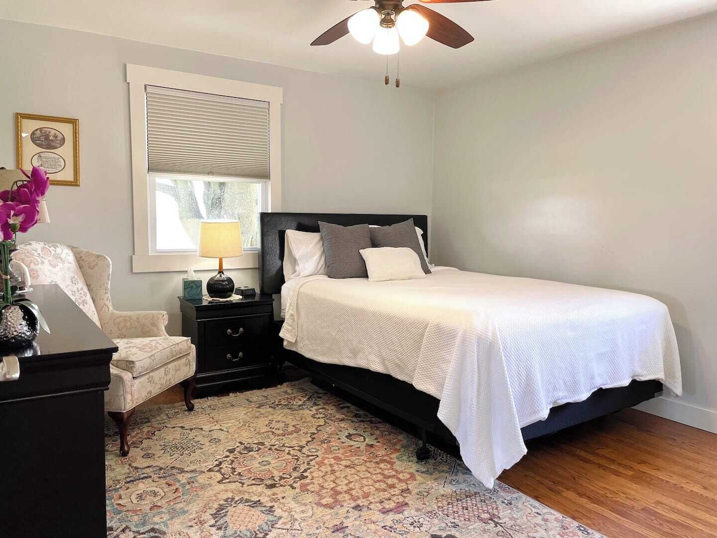 Une chambre à coucher comprenant un lit, une table de chevet, une lampe, une chaise et un ventilateur de plafond.