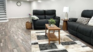 Un salon moderne avec deux canapés en cuir noir, une table basse en bois, un tapis à motifs et une petite table d’appoint avec une lampe.