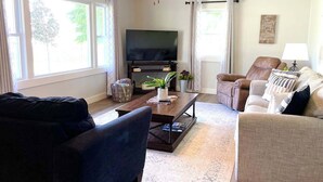 Un salon doté d’un ventilateur de plafond, d’un téléviseur à écran plat, d’un canapé, d’une table basse et d’une fenêtre avec des rideaux.