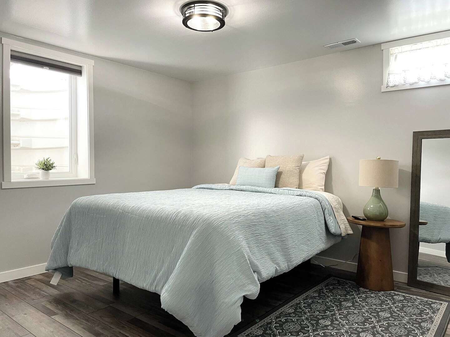 Un dormitorio con cama, mesita de noche, lámpara, ventana y espejo.