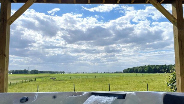 Un bain à remous avec vue sur un champ verdoyant et un ciel nuageux.