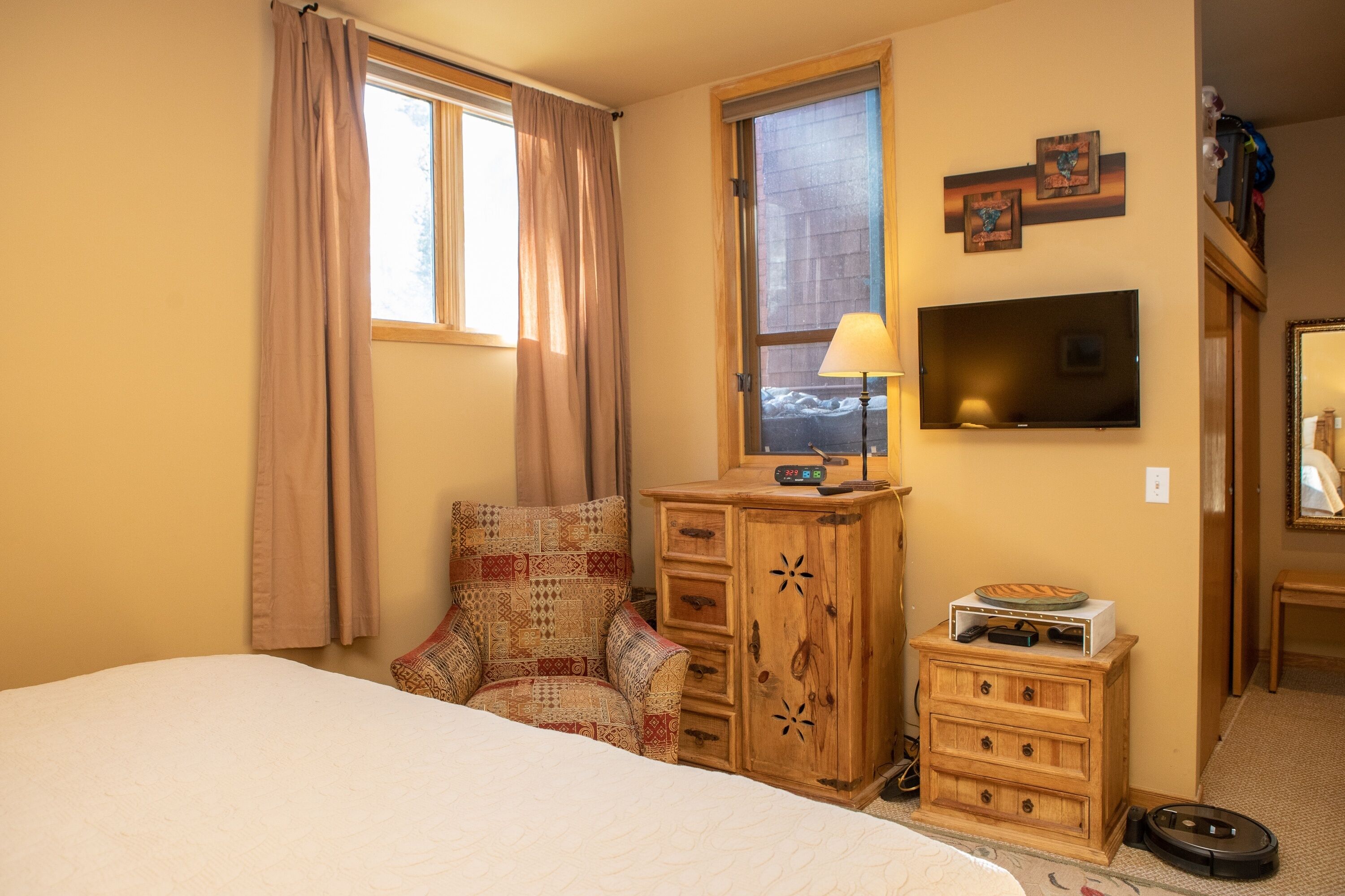 Une chambre d’hôtel avec un lit, une commode en bois, une télévision et une fenêtre avec des rideaux.