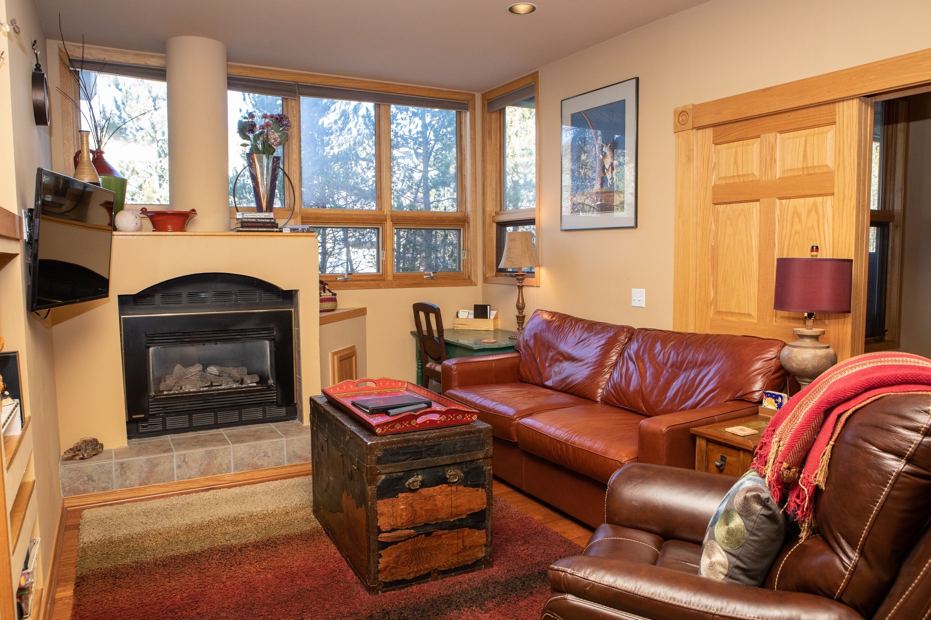 A cozy living room with a fireplace, leather sofa, and a rustic chest of drawers.