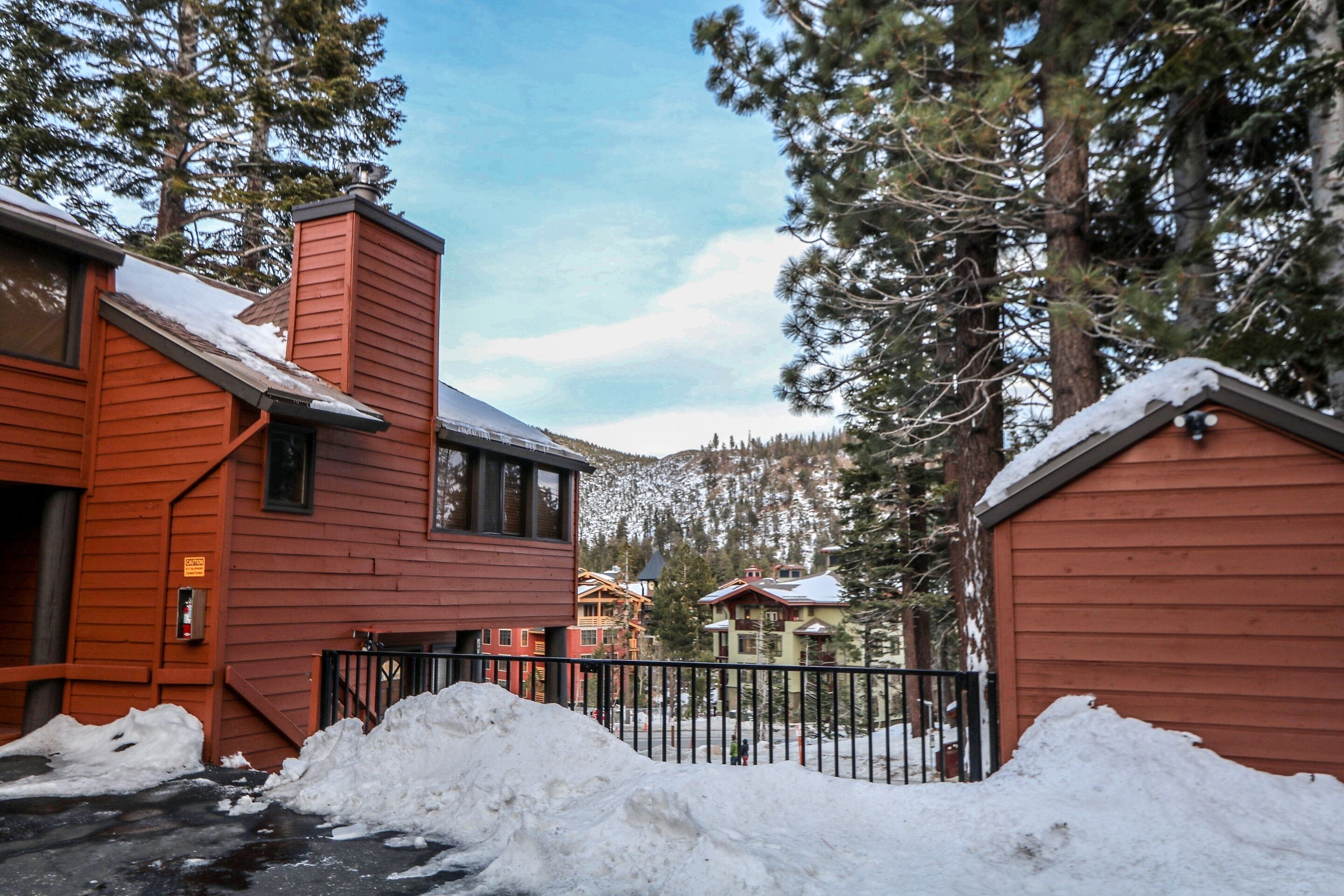 A red building with a snow-covered roof, surrounded by trees and a wooden fence.