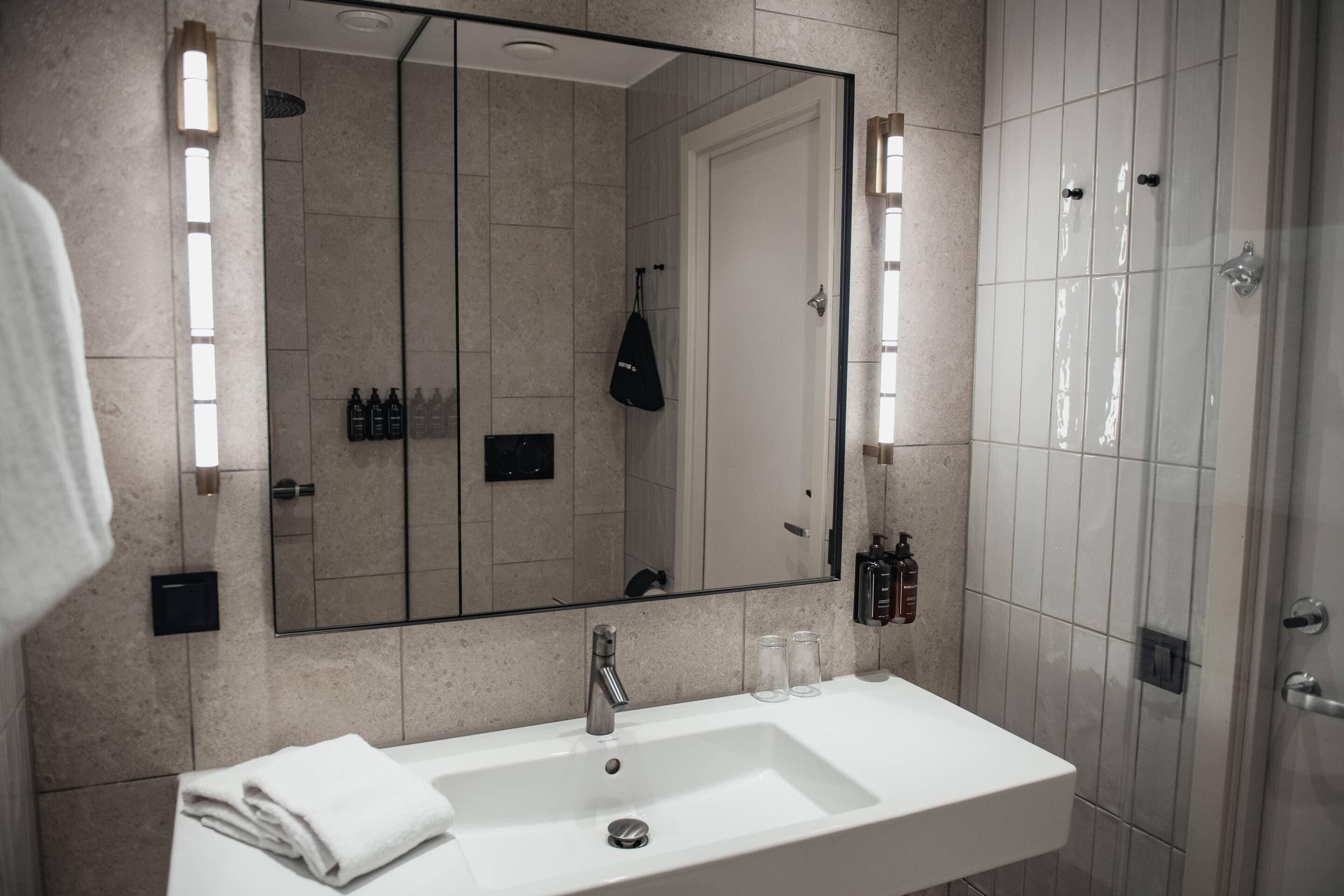 A bathroom with a large mirror, a white sink, a towel, and a shower area.