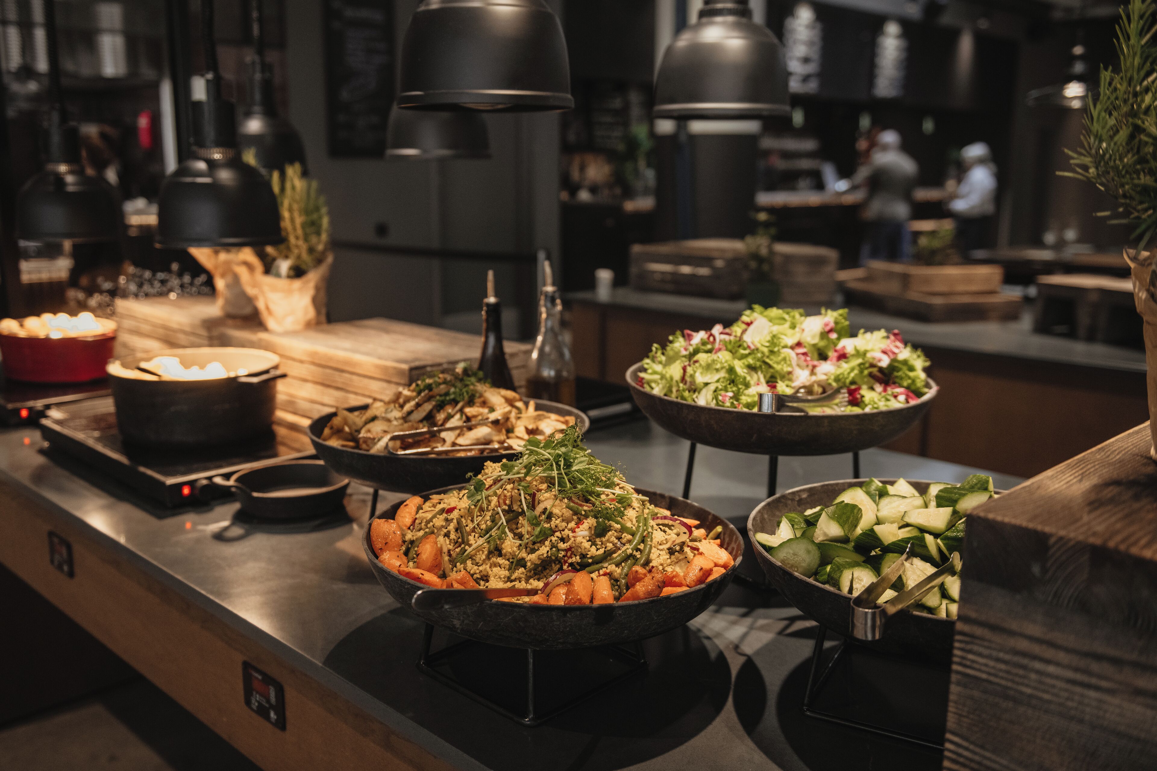 Un bufé con diversos platos, entre ellos ensaladas, verduras y una olla grande.