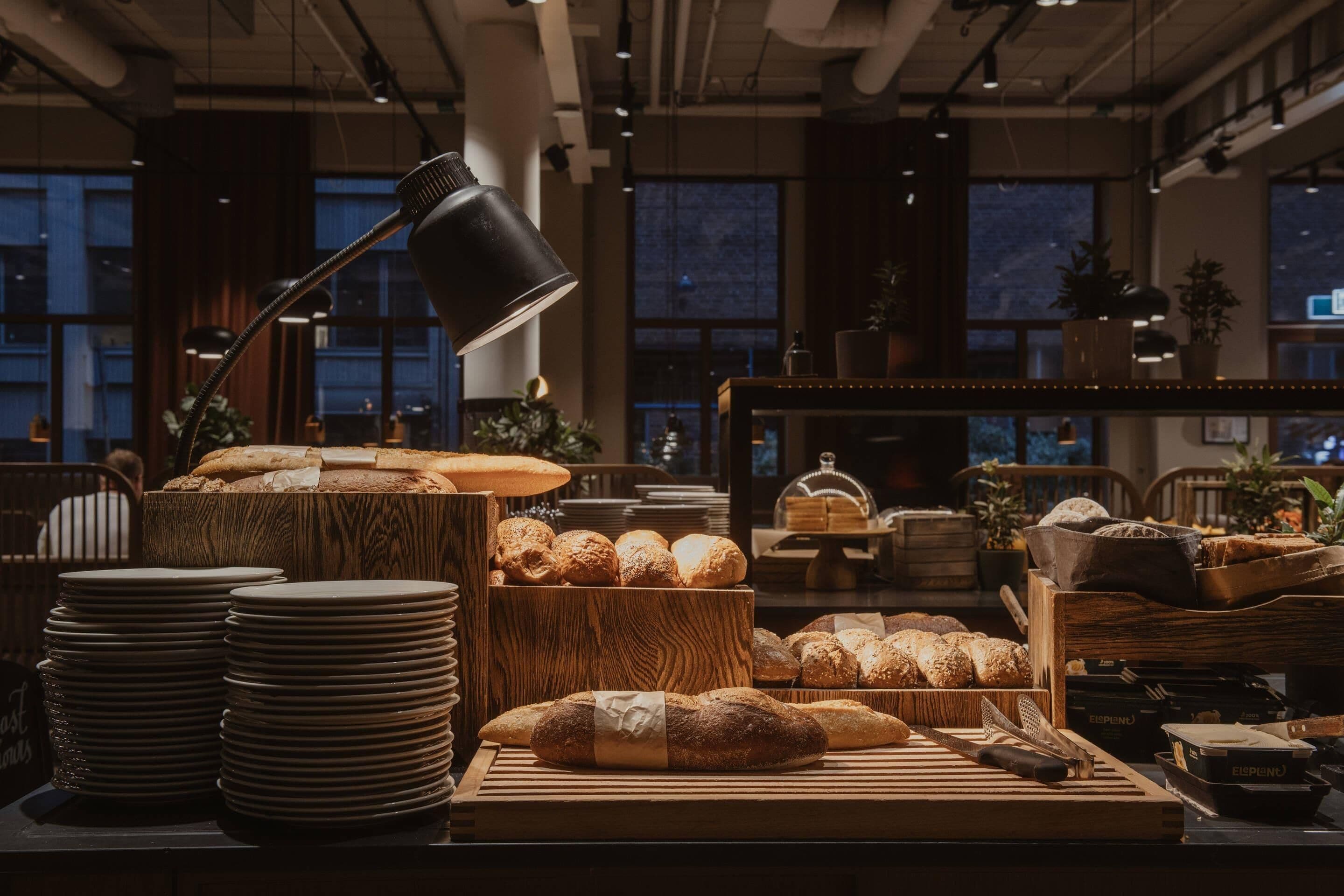 A bakery display with various breads and pastries, wooden tables, and a lamp.