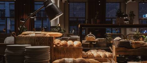 A bakery display with various breads and pastries, wooden tables, and a lamp.