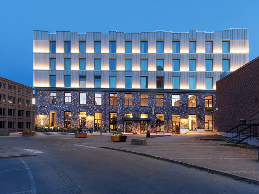 A modern building with multiple floors, large windows, and a well-lit entrance area with outdoor seating.
