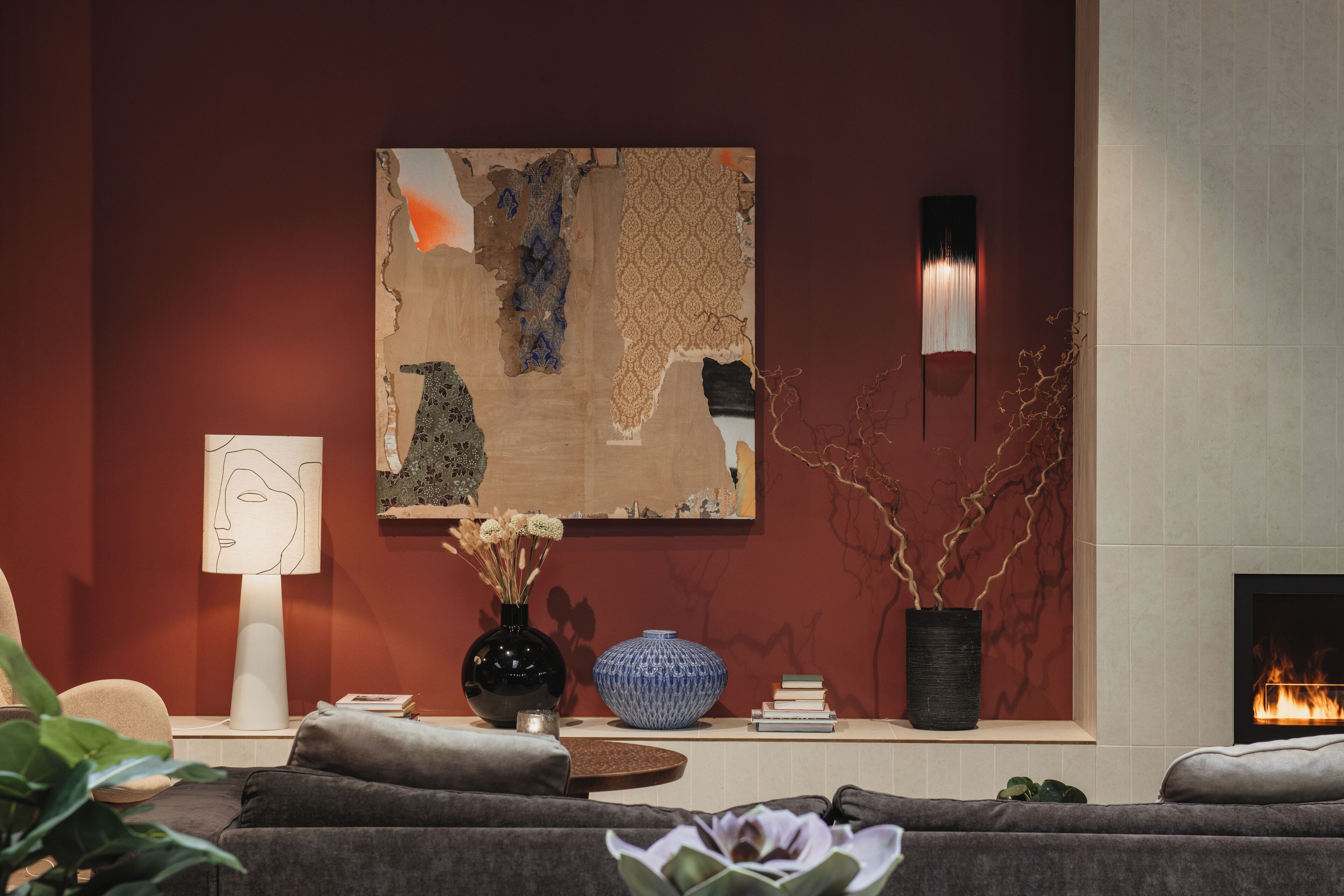 A modern living room with a fireplace, a large abstract painting, and a vase with flowers.