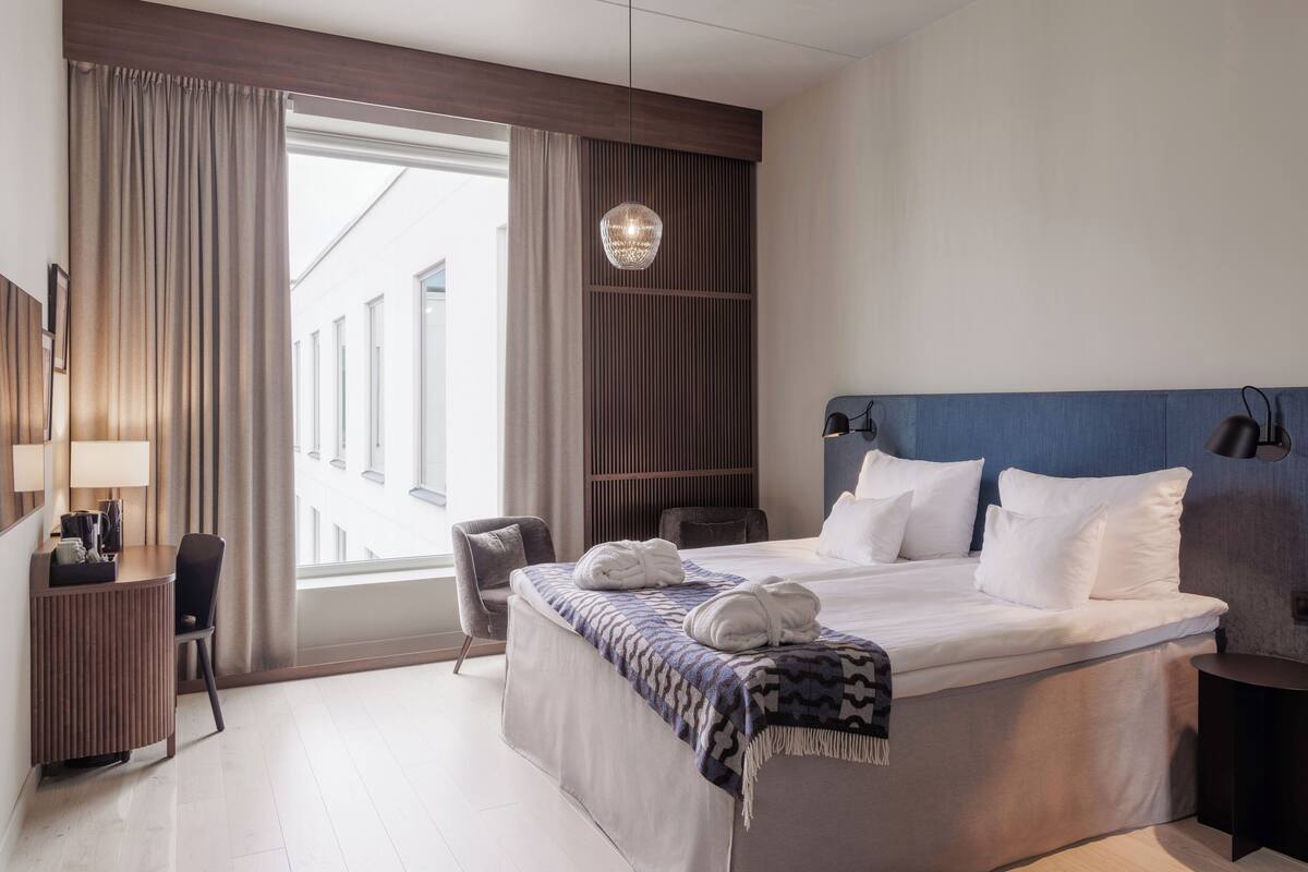 Habitación de hotel moderna con una cama grande, un escritorio, una silla y vistas a la ciudad.