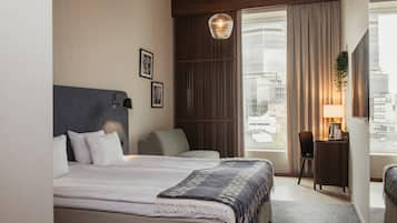 A hotel room with a bed, a desk, a chair, a hanging light fixture, and a view of the city.