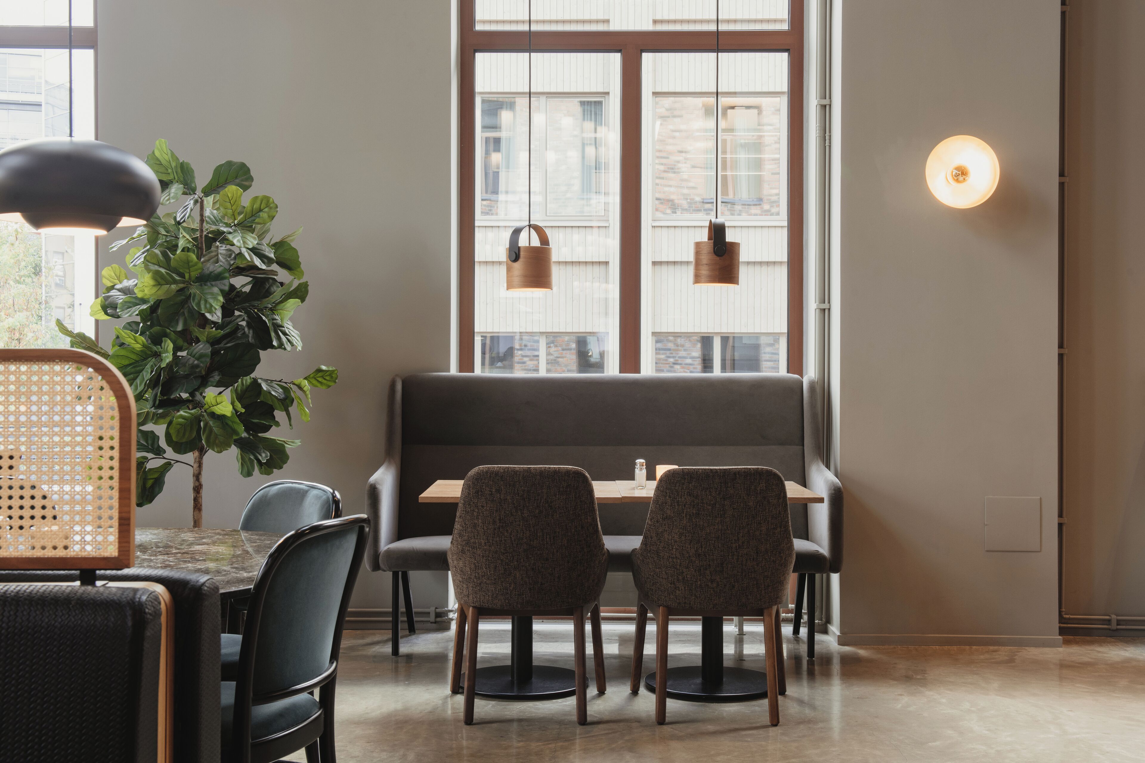 Un comedor con una mesa, sillas, un banco, una planta en maceta, luces colgantes y una lámpara fijada a la pared.