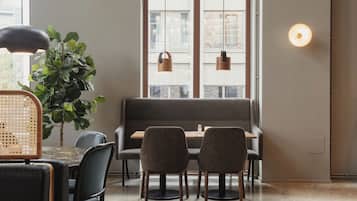 Un comedor con una mesa, sillas, un banco, una planta en maceta, luces colgantes y una lámpara fijada a la pared.