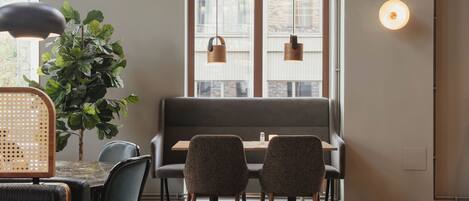 Un comedor con una mesa, sillas, un banco, una planta en maceta, luces colgantes y una lámpara fijada a la pared.