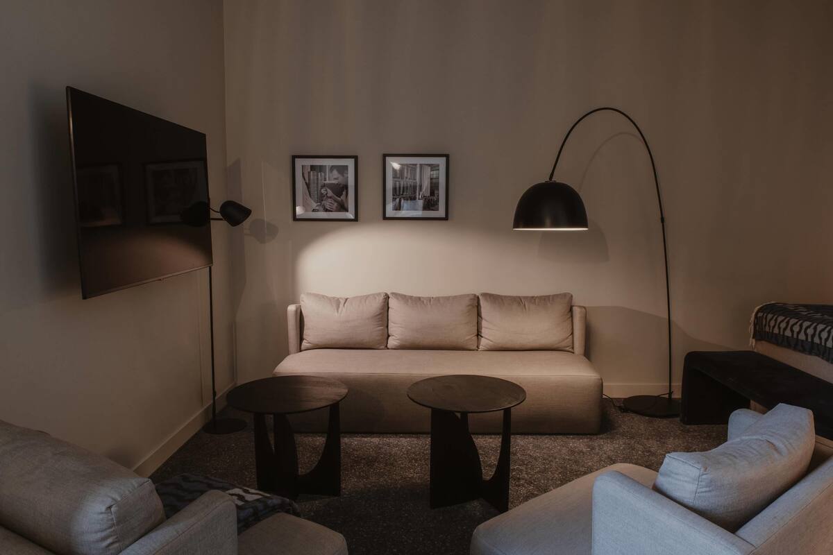 Una sala de estar con un sofá, dos mesas auxiliares, una lámpara de pie y cuadros enmarcados en la pared.