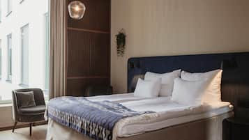 A hotel room with a large bed, a chair, a hanging plant, and a view of the outside.