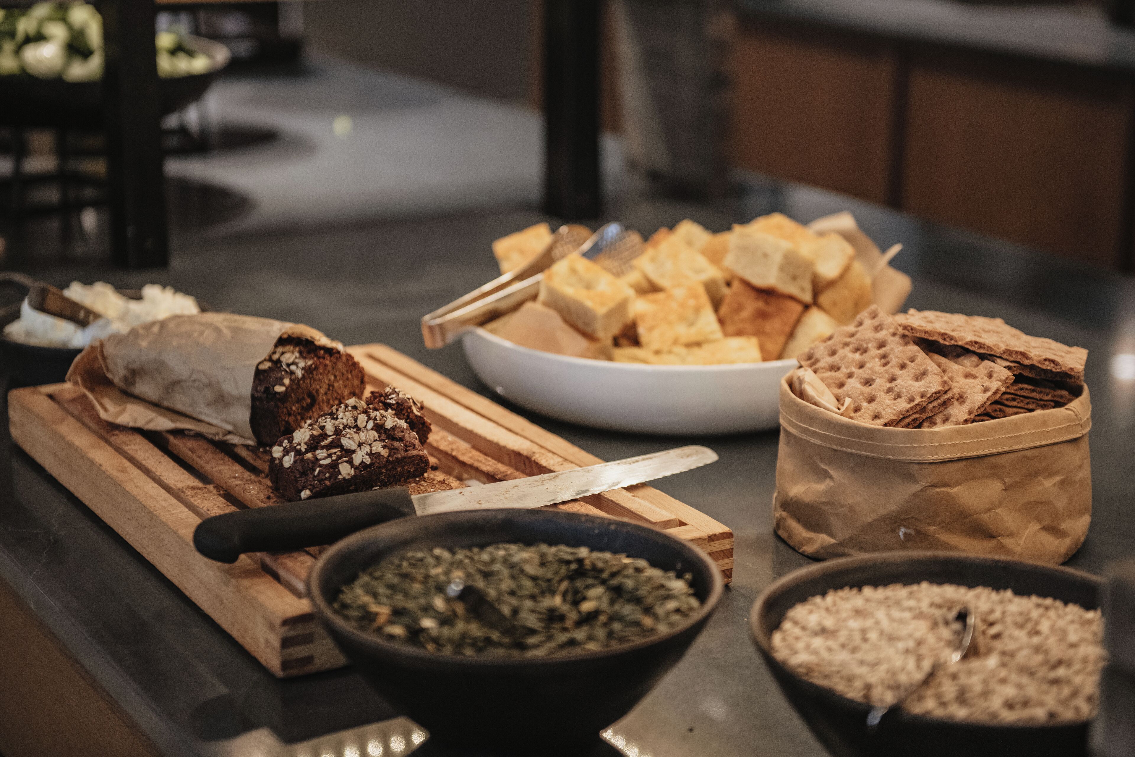 Un piano di lavoro della cucina con diversi alimenti, tra cui pane, cracker e ciotole piene di semi.