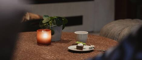 A table with a candle, a small plant, and a plate with a dessert.