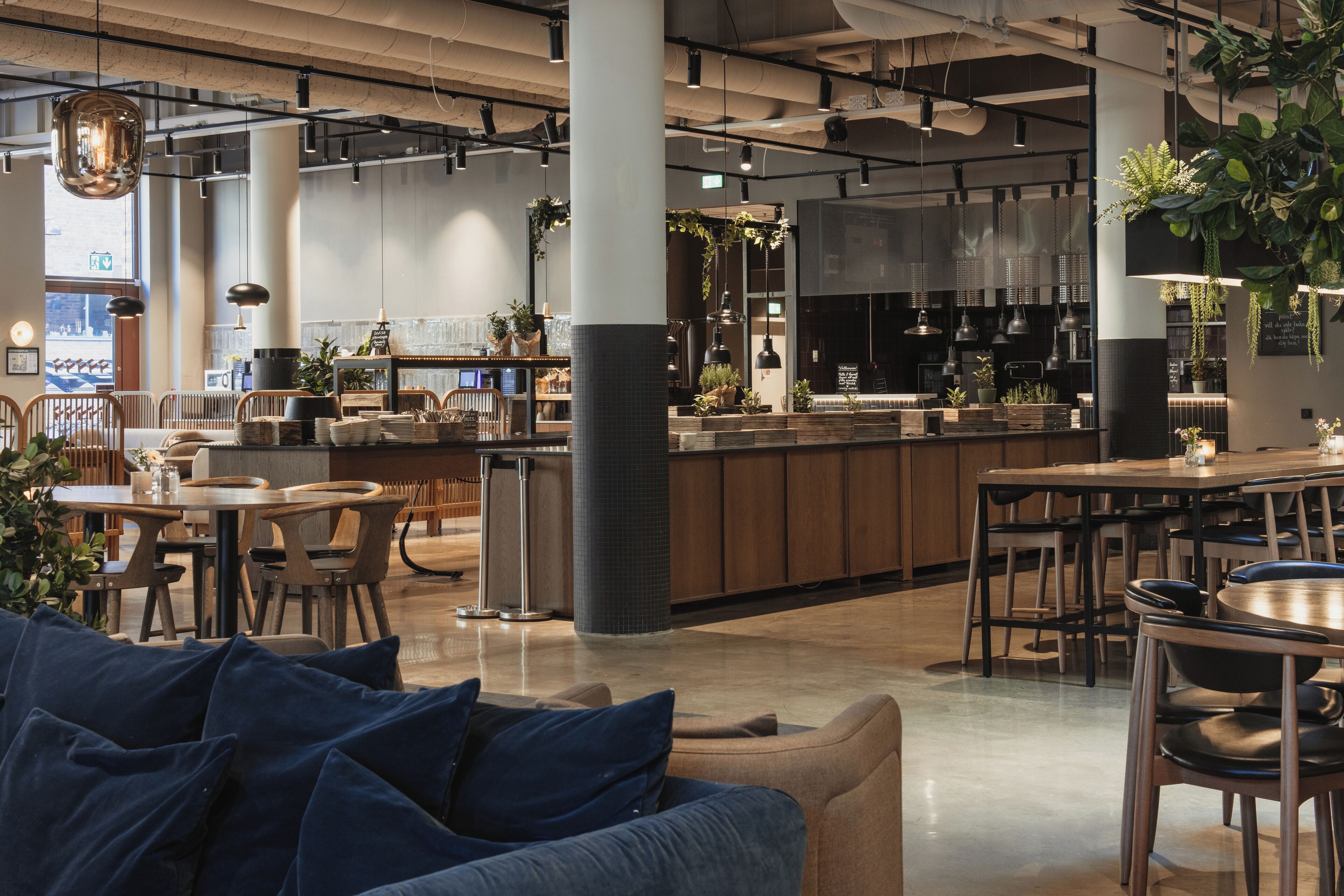 A modern interior with a central bar area, seating arrangements, and indoor plants.