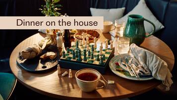 A cozy dining setup with a chessboard, a cup of tea, and a plate of food on a round table.