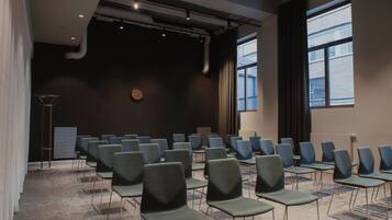 Una sala de conferències amb files de cadires, un rellotge a la paret i grans finestres.