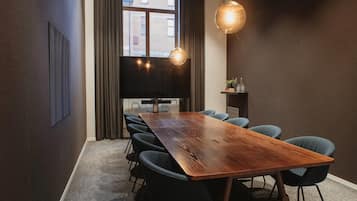 A conference room with a long wooden table, six chairs, a flat-screen TV, and pendant lighting.