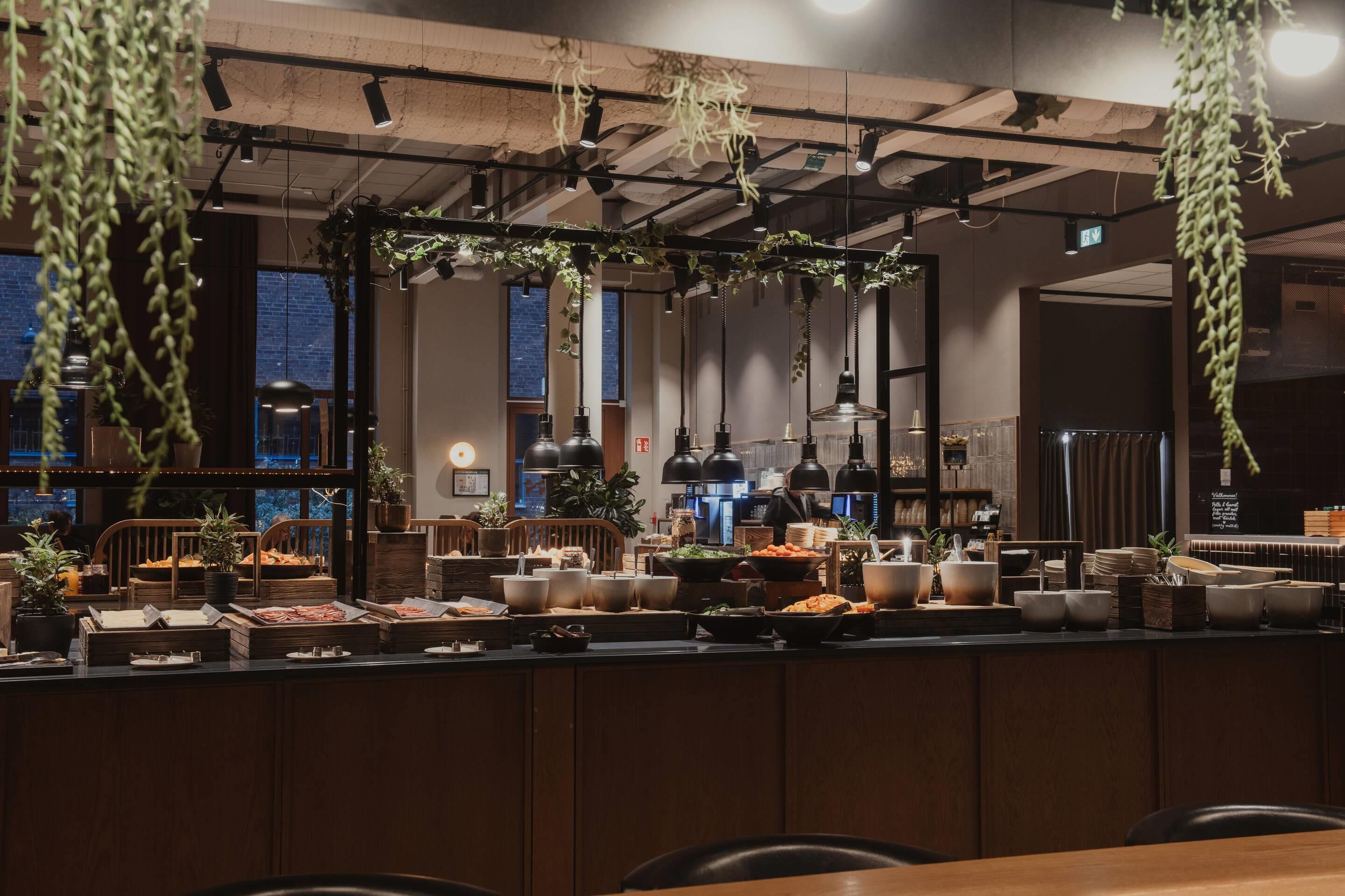 A restaurant with a long counter, hanging plants, and a view of the city.