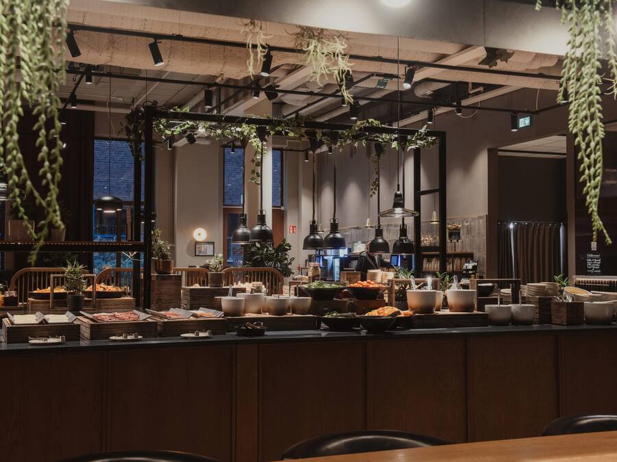 A restaurant with a long counter, hanging plants, and a view of the city.