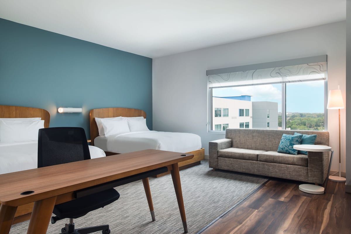Een hotelkamer met een bed, een bureau, een stoel, een bank en een raam met uitzicht op gebouwen.