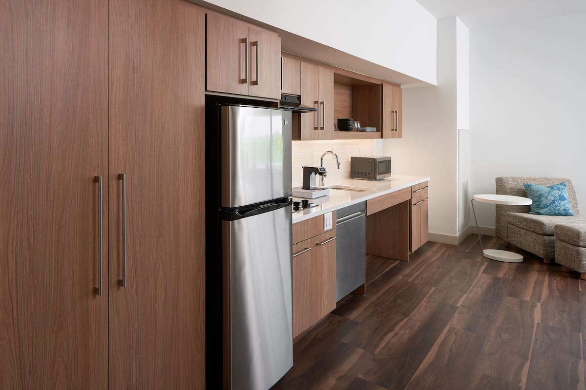 Een moderne keuken met houten kastjes, roestvrijstalen apparatuur en een zithoekje met een ronde tafel en kussens.