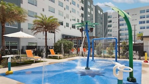 A swimming pool with water jets, palm trees, and lounge chairs. - Element by Marriott Orlando at SeaWorld (Orlando)
