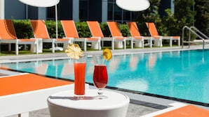 A poolside area with lounge chairs and a table with two drinks. - Element by Marriott Orlando at SeaWorld (Orlando)