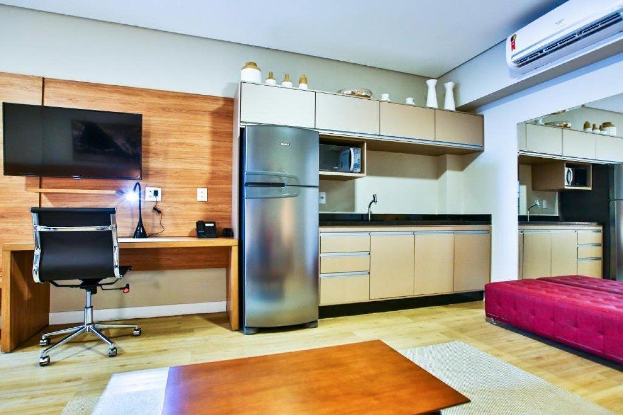 A compact kitchen with a refrigerator, microwave, and a flat-screen TV mounted on the wall.