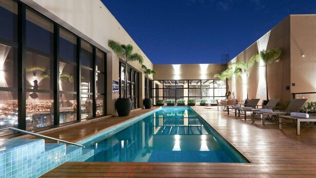 A modern indoor pool area with a long pool, lounge chairs, and potted plants. - Comfort Suites Sao Jose do Rio Preto (São José do Rio Preto)
