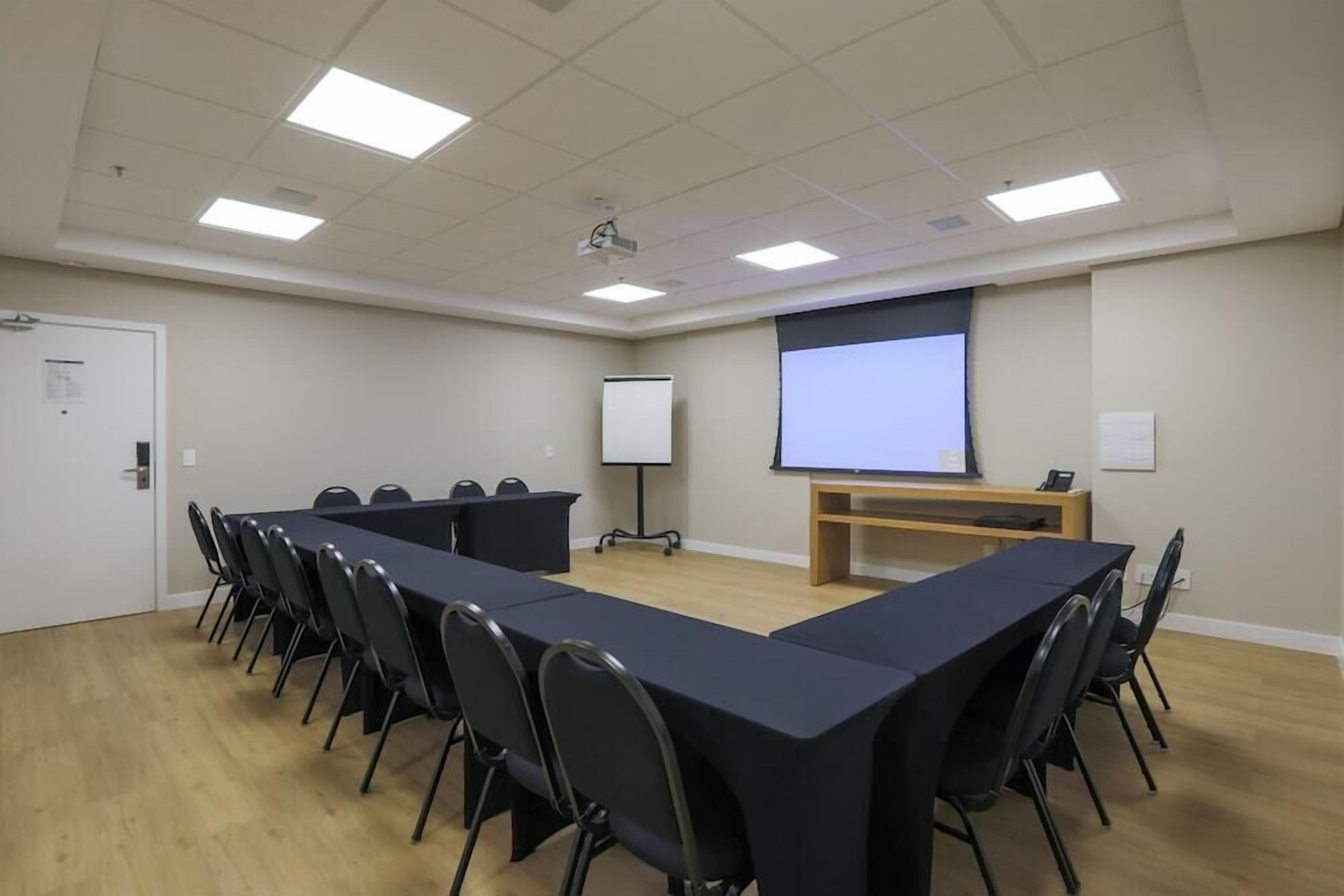 Ein Konferenzraum mit einem langen Tisch, Stühlen, einer Projektionsleinwand und einer Whiteboard-Tafel.