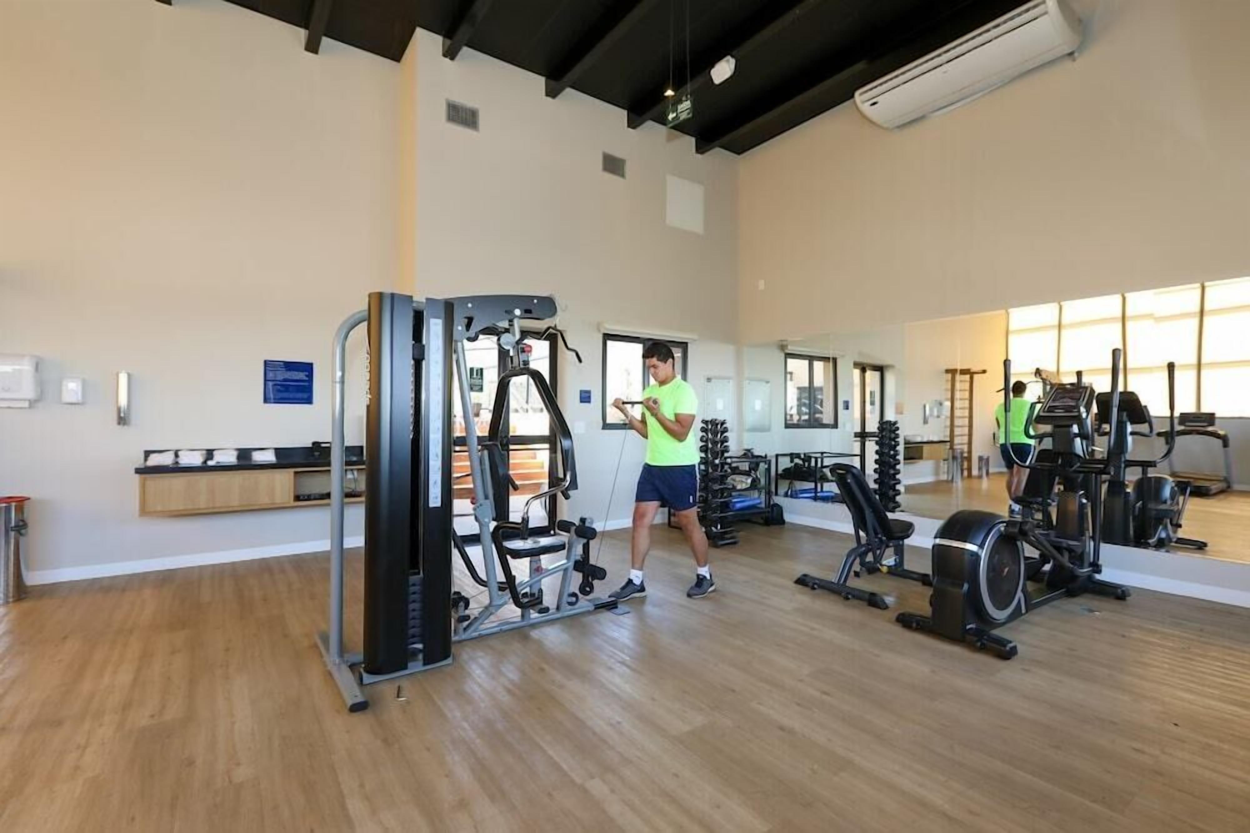 Uma academia com equipamentos de ginástica, piso de madeira e uma grande janela.