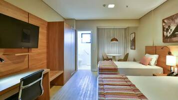A hotel room with a TV, a desk, a bed, a bedside table, a lamp, and a window with curtains.