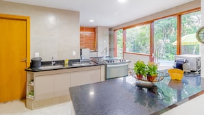 A modern kitchen with a central island, a stove, and a sink. There are potted plants on the island and a window with a view of trees.