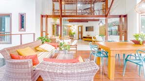 A spacious living area with wicker furniture, a wooden dining table, and blue chairs.