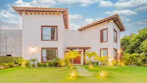 A modern two-story house with a well-maintained lawn, a pathway leading to the entrance, and a variety of tropical plants.