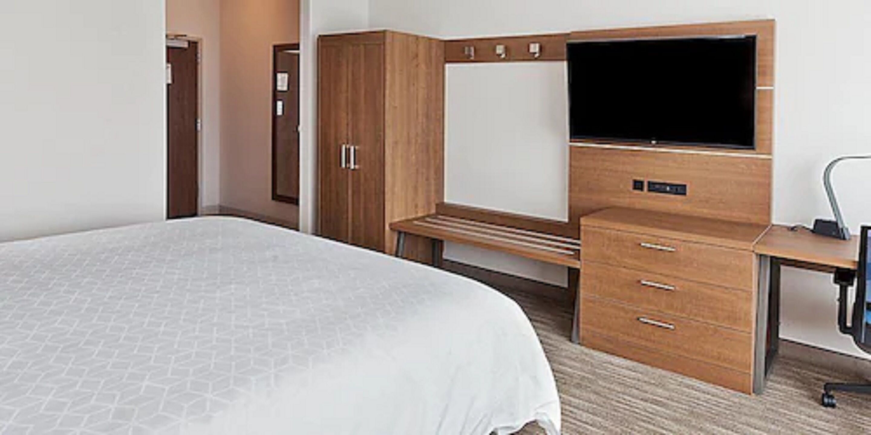 A hotel room with a bed, a desk, a television, and a wardrobe.