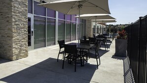 An outdoor patio with tables and chairs, large umbrellas, and a stone building facade. - Holiday Inn Express and Suites Griffin by IHG (Griffin)