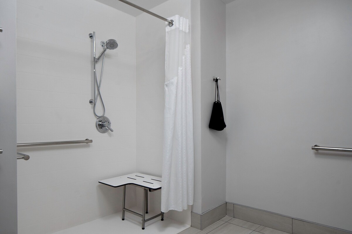 A modern bathroom with a shower, a white towel rack, and a small bench.