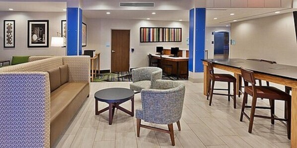 A modern hotel lobby with a sofa, armchairs, a round table, and a dining area. - Holiday Inn Express and Suites Griffin by IHG (Griffin)