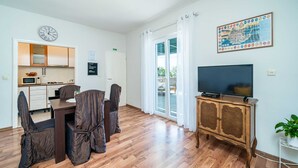 A modern living room with a dining area, a flat-screen TV, and a large window with curtains. - Apartments Nico (Dubrovnik)