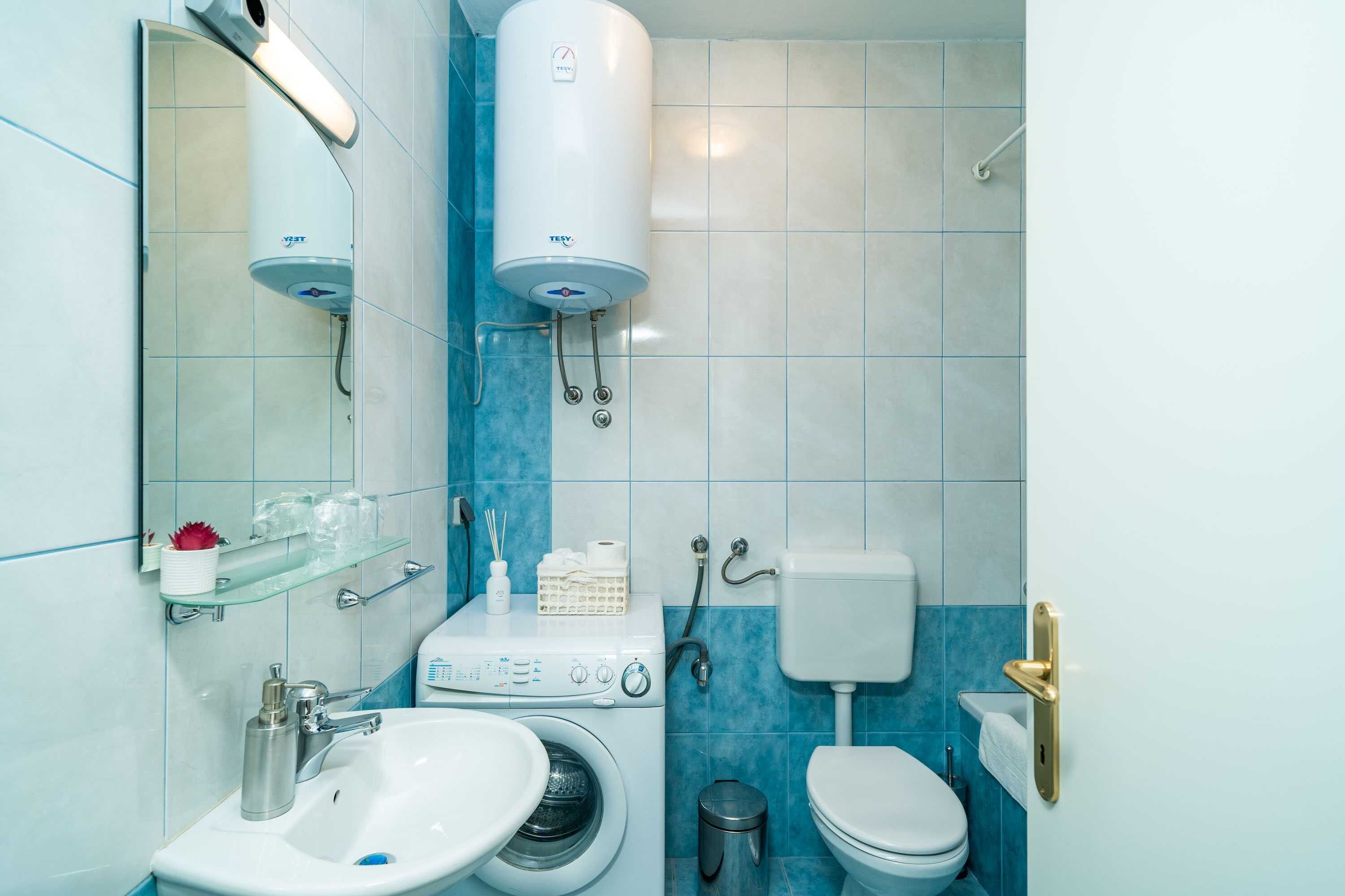 Ein kleines Badezimmer mit Waschbecken, Waschmaschine, Toilette und Warmwasserbereiter.