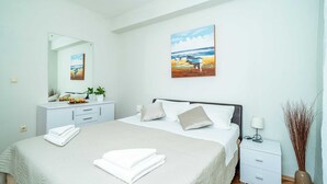 A neatly arranged bedroom with a bed, bedside table, and a painting of a beach scene. - Apartments Nico (Dubrovnik)