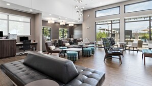 A spacious lounge area with a grey sofa, multiple seating options, and large windows offering a view of the outdoors. - Residence Inn by Marriott Port Arthur (Port Arthur)
